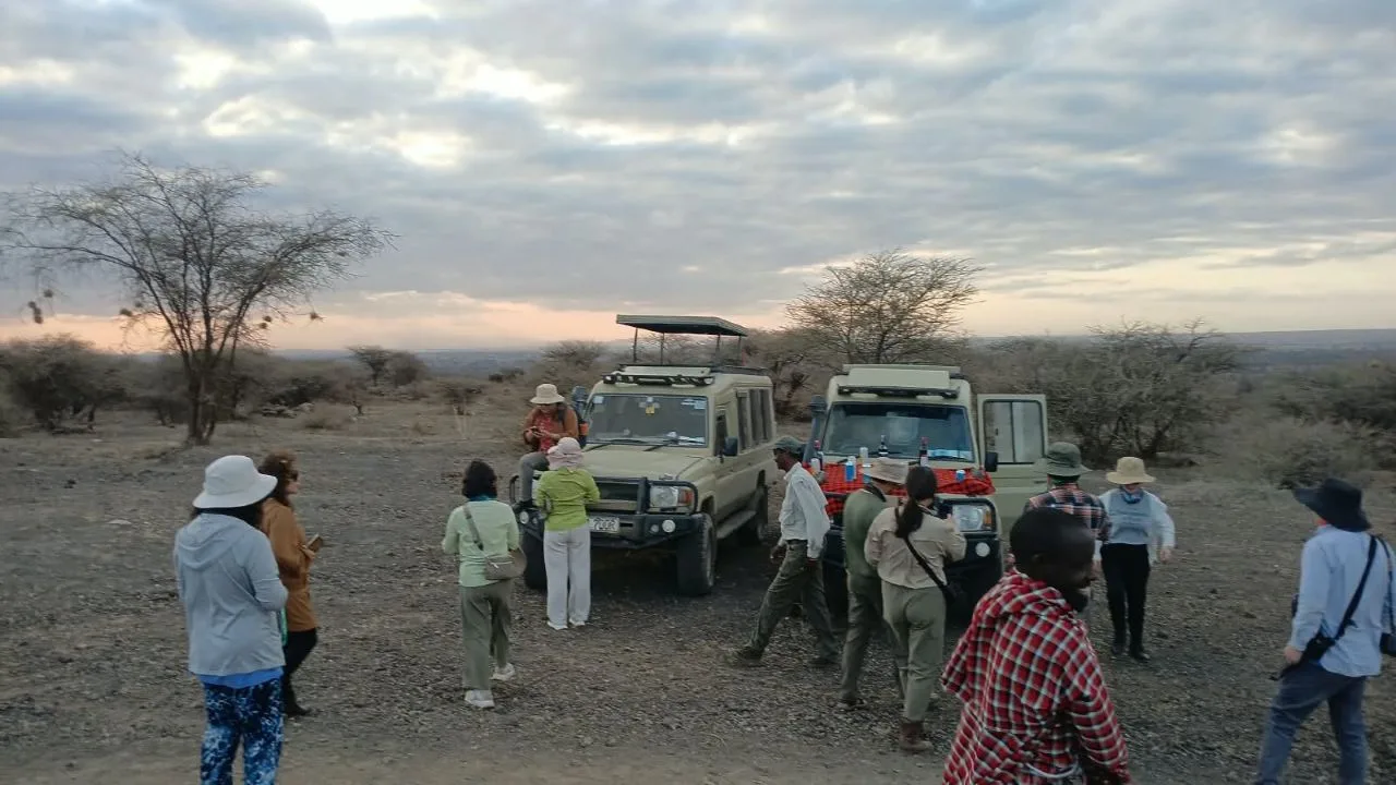 Guests enjoying a Kenya safari sundowner beside two 4x4 Land Cruisers